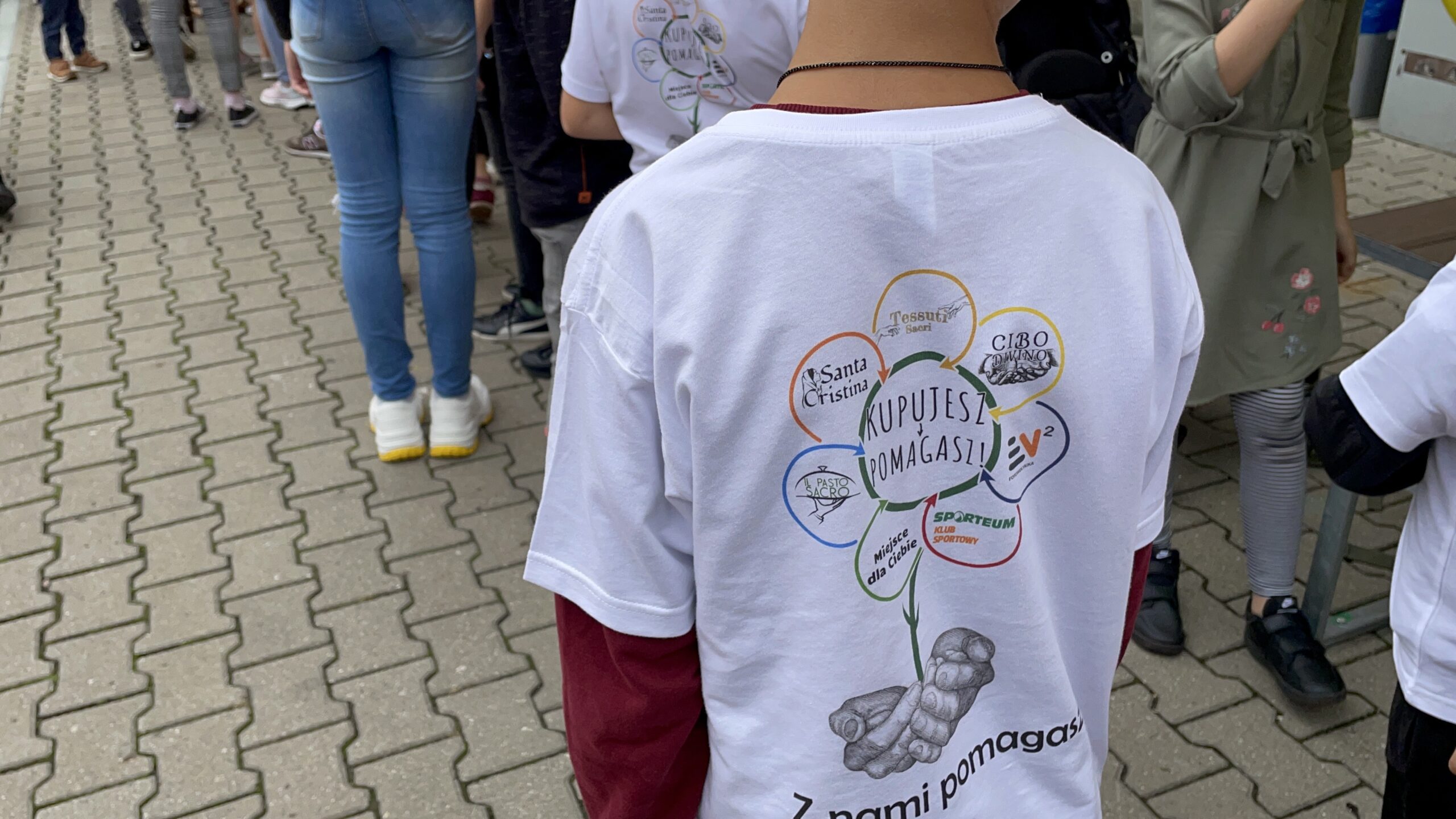 Logotypy firm na płatkach kwiatu. Koszulka akcji z napisem „Z nami pomagasz” i logotypami firm, które wspierają inicjatywę.