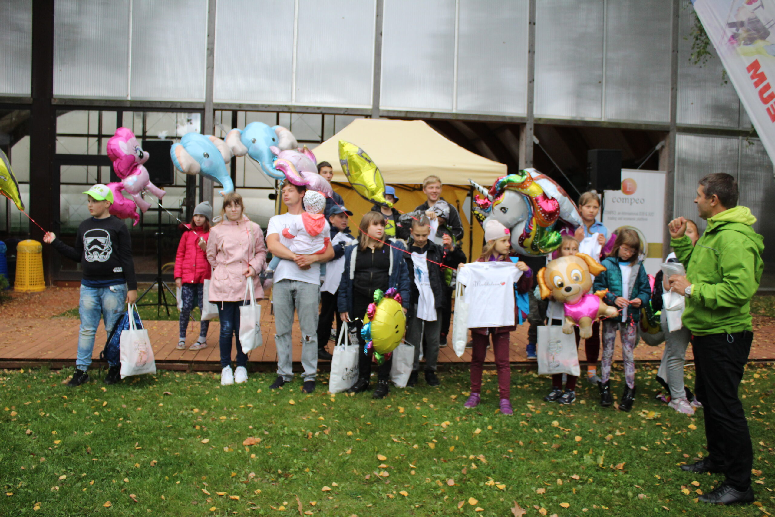 Upominki dla uczestników. Dzieci i młodzież z balonami, torbami i koszulkami z akcji, wspólne zdjęcie na trawniku.
